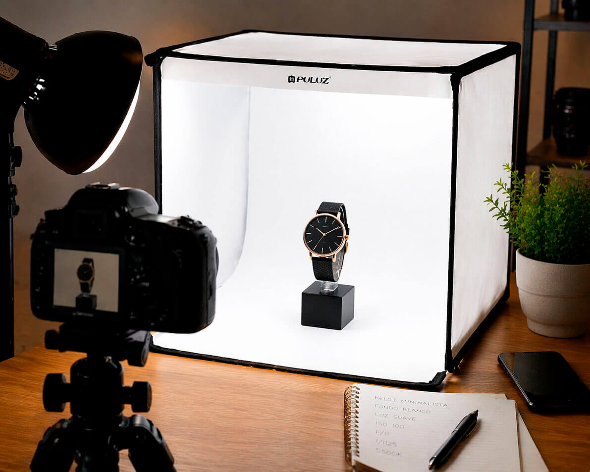 Set de fotografía de producto con caja de luz, cámara y reloj sobre fondo limpio