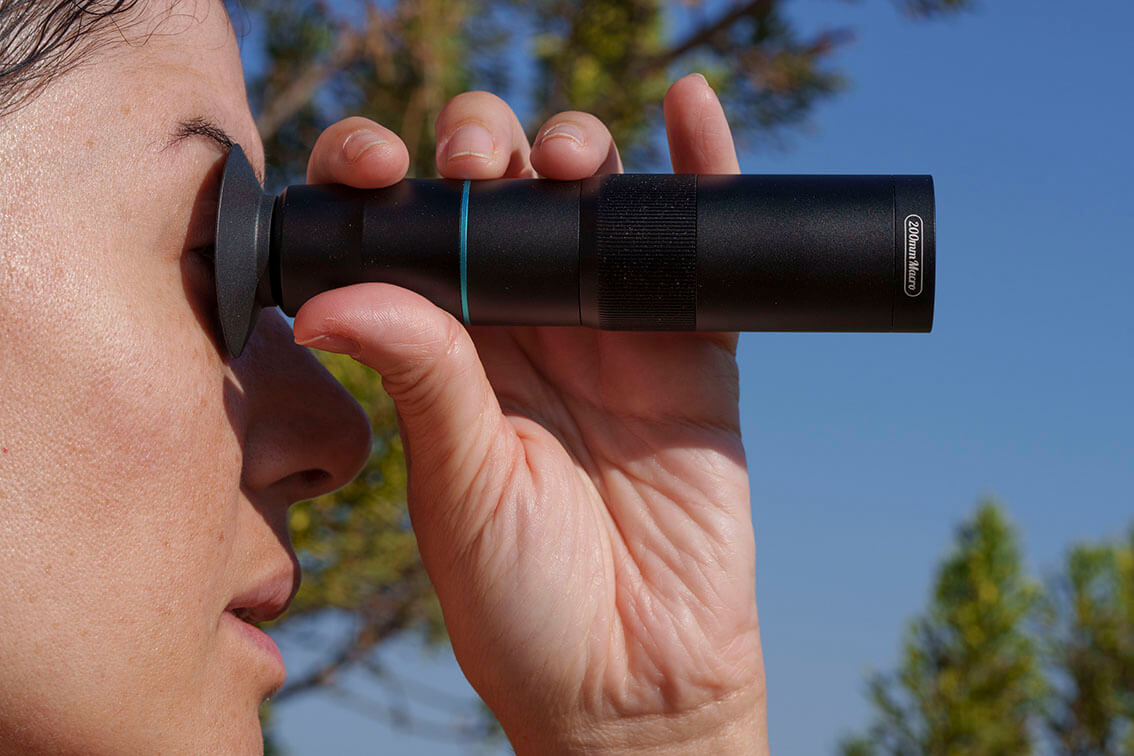 Persona utilizando un teleobjetivo APEXEL como monocular en exteriores